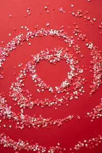Top view of small confectionery topping scattered on surface and forming heart shape on bright...