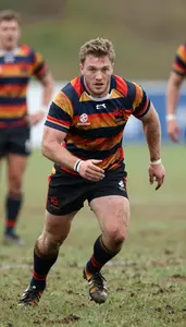 Rugby Player In Striped Kit Charging Forward Across A Muddy