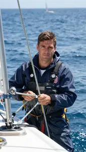 Sailor In Waterproof Jacket Adjusting Sail Ropes On Windy