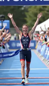 Triathlete In A Trisuit And Race Belt Crosses The Finish