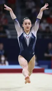 Gymnast In Sleek Attire Performing A Twisting Leap On Floor