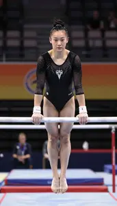 Gymnast In A Black Leotard Performs On The Uneven Bars