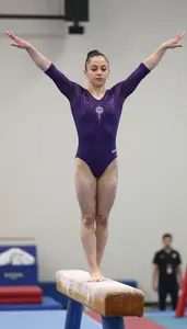 Gymnast In A Deep Purple Leotard Balances On The Beam On One