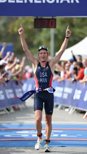 A Triathlete In A Trisuit And Race Belt Crosses The Finish