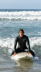 A Surfer In A Wetsuit Sits On Their Board In The Lineup