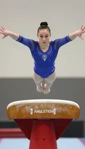 Gymnast In A Blue Leotard Performs On The Vault Mid Flight