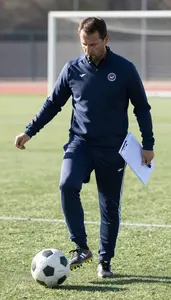 Soccer Coach Kicking A Soccer Ball On A Soccer Field During Practice In