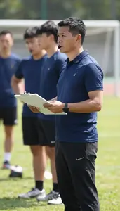Sports Coach Managing A Team From On A Sports Field During Practice In