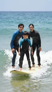 Family Surfing Together Trying To Catch A Wave In Matching Wetsuits