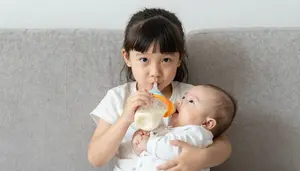 Little Girl Feeding Her Baby Sibling A Bottle On The Couch