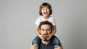 Child Pulling Fathers Beard While Sitting On His Shoulders Laughing