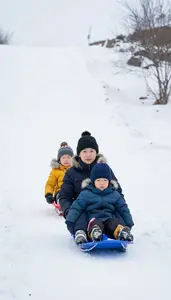 Family Bundled Up In Coats Sledding Down A Steep Snowy Hill