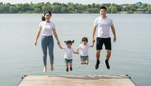 Family Holding Hands And Jumping Off A Dock Into A Lake