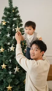 Father Lifting Child To Hang Star On Tree