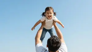 Father Lifting His Laughing Daughter Up Towards A Bright Blue Sky