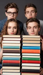Four Friends Peeking Over A Stack Of Colorful Vintage Books