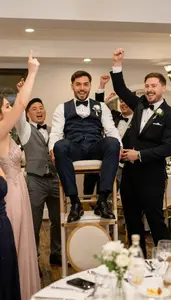 Friends Cheering And Lifting A Groom On A Chair At A Wedding Reception